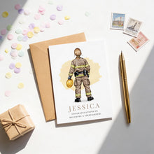 a card with an illustration of a firefighter, a gift box, and some scattered confetti on a white surface.