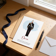 A card with a drawing of a person in a military uniform, along with a pen and an envelope on a wooden desk.