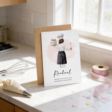 a card with an illustration of a woman holding a cake and a chef's hat, placed on a kitchen counter.