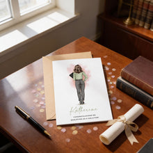 A greeting card with a woman illustration and the name "Katherine" printed on it, placed on a wooden desk with a pen, a rolled-up diploma, and some books.