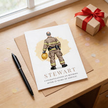 a card with a firefighter illustration and a gift box with a red ribbon on a wooden surface.