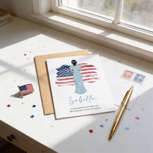 a greeting card with a woman standing in front of an American flag, along with a pen, a postcard, and some confetti on a desk.