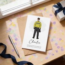 A greeting card with a police officer illustration is placed on a wooden surface, surrounded by confetti and a gift box.