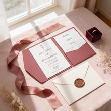 A wedding invitation card from the couple, a wedding envelope, a wedding ring box, and a wax seal are arranged on a pink tablecloth.