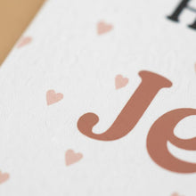 a close-up of a white surface with a large brown letter "J" and smaller pink heart shapes scattered across it.