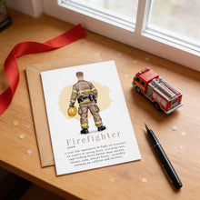 a card with a firefighter illustration, a toy fire truck, and a pen on a wooden surface.