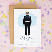 A greeting card with an illustration of a person in a military uniform, likely a sailor, and the name "Sebastian" written on it. The card is placed on a background of colorful confetti.