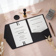 A wedding invitation card with the names Elinor & Robert, along with details about the wedding and guest information, is displayed on a table with a wedding ring box, a pen, and some dried flowers.