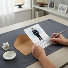 A person's hands are holding a pen and writing on a card with an illustration of a uniformed person, which appears to be a wedding invitation.